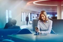 Business woman with tablet looking at her phone. Primary color: blue.