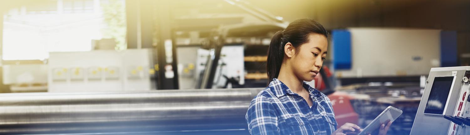 Female Asian factory worker operating a touch-screen display. Hair in a ponytail. Checkered shirt. Primary color blue.